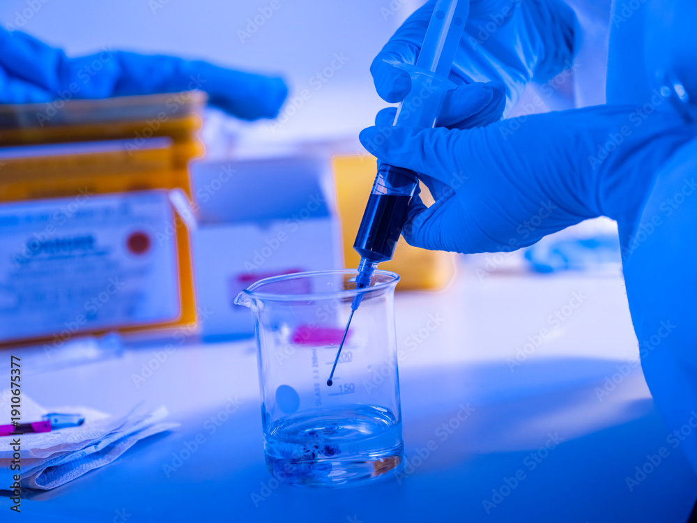 Fototapeta premium Alternative angle of syringe and beaker laboratory procedure with blue dramatic lighting capturing analytical chemistry process