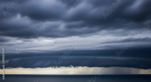 Dark storm clouds gather over sea, rain falls on horizon