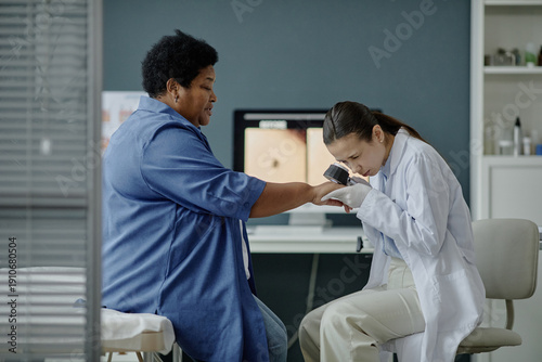 Foto Young Asian woman dermatologist examining hand of middle aged Black woman using