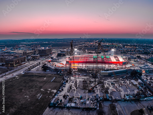 Aerial view of a vibrant stadium glowing with bright red and white lights against the dusky sky, Frisco, Texas, United States.