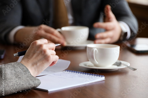 People talking at the table with tea cups, woman with pen and man in business suit. Concept of business meeting, discussion, interview
