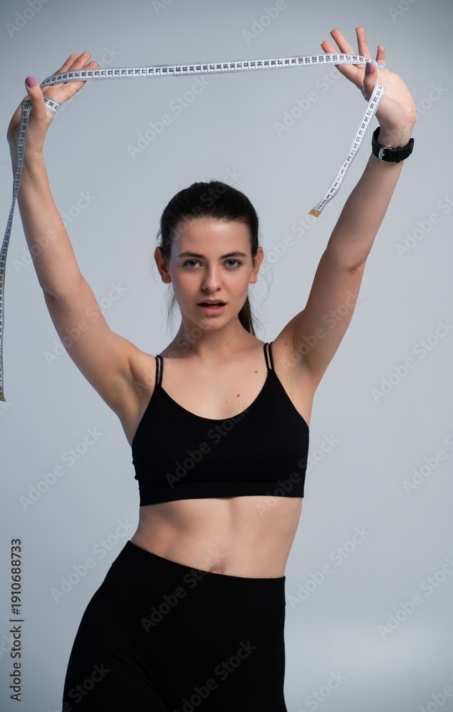Obraz premium Woman in sportswear holding a tape measure above her head, symbolizing weight loss progress, fitness goals, measuring healthy lifestyle achievements, body care, and diet success