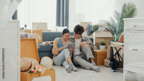 Young happy Asia couple sit on sofa couch use digital tablet online shopping furniture from decoration store in living room at home. Husband wife move new house, Apartment Rent And Ownership Concept.