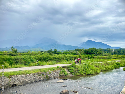 Peaceful Rural Road Beside Small River with Mountain Background