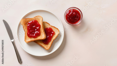 Two slices of golden toast with strawberry jam on white plate next to glass jar and knife breakfast or snack concept on light background
