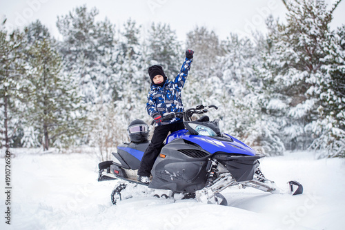 фотографія Boy on the snowmobile up in the mountains smiling in a snowy weather, forest