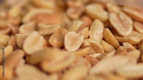 A tight macro close-up of roasted peanuts, some whole and some split into halves. The nuts are warm golden-brown with a slightly oily sheen and visible salt crystals.