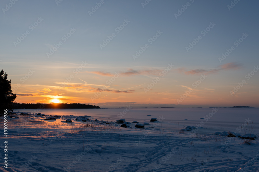 Obraz premium Winter sunset over a frozen sea with snow-covered shore and distant islands