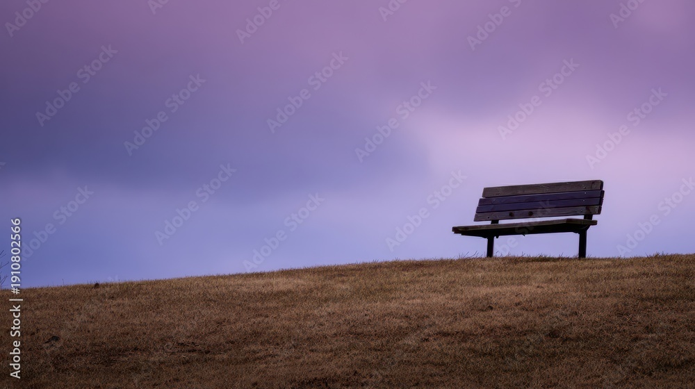 Fototapeta premium A solitary wooden park bench rests on a hilltop, bathed in a tranquil, purple-tinged twilight.