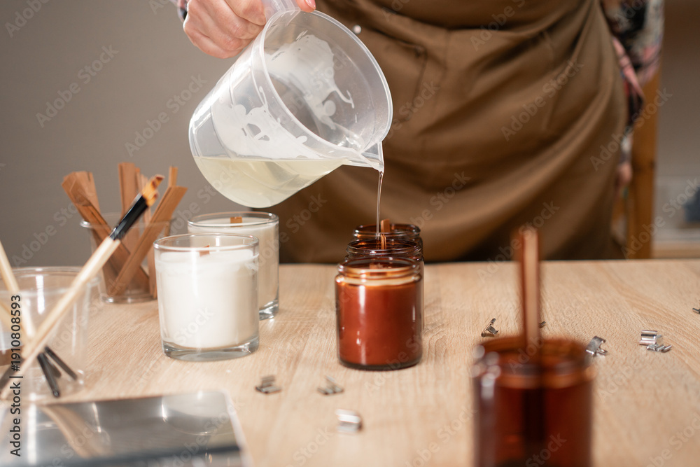 Naklejka premium Creative hobby as Handmade soy wax candle in workshop. Close-up of woman pouring liquid wax into the mold.