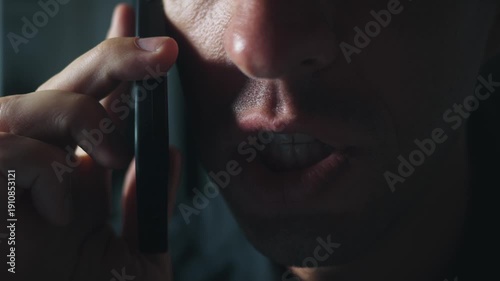 Extreme closeup angry millennial man shouting into smartphone in dark dramatic light. Concept aggression rage conflict toxic communication stress dominance emotional pressure modern male confrontation