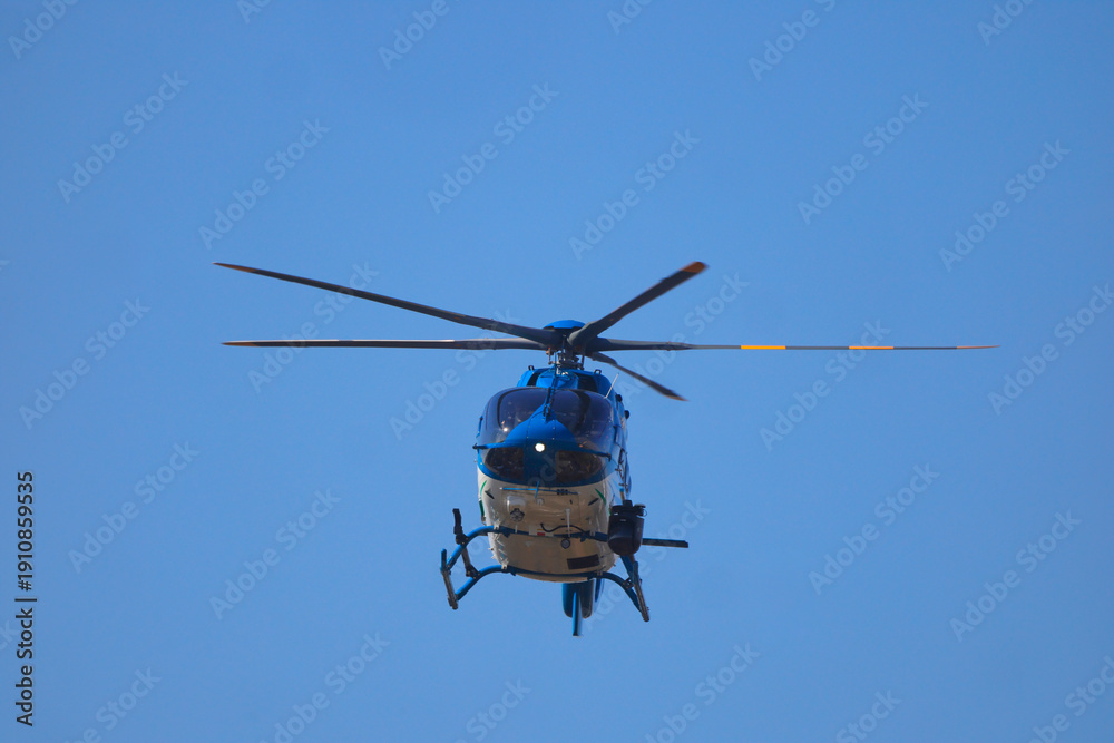 Fototapeta premium Blue and white helicopter inflight on patrol against clear blue sky. 