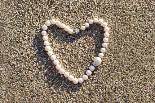 Concept of love and health. Pearl necklace arranged in the shape of a heart on sandy surface during daylight