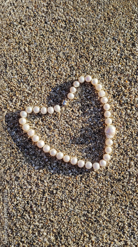Creating a heart shape on sand using small round beads to express love in a coastal setting during daytime. Concept of love and health
