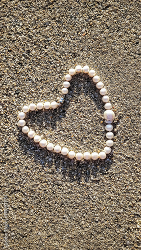 Heart shape made of pearls placed on a sandy surface during daylight shows a simple yet meaningful symbol of love and connection for special occasions