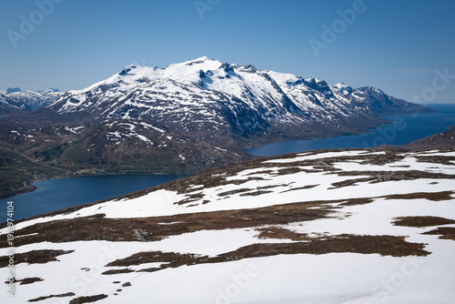 Wide view from Rødtinden mountain on Kvaløya island shows deep blue fjords curving between rugged slopes and distant snow covered peaks near Tromsø in Northern Norway