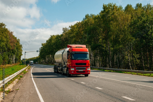 A red truck with a tanker is driving along the highway