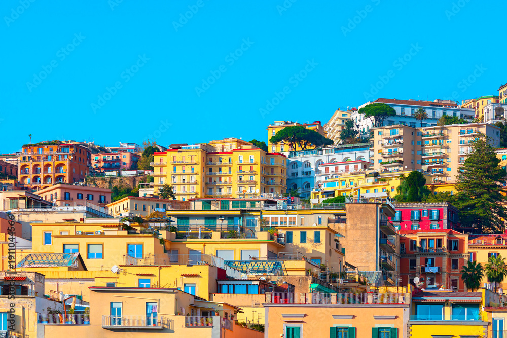 Fototapeta premium Pastel colored houses of the Vomero district in Naples, Italy, nestled on a steep hillside. Dense Mediterranean architecture under blue sky. Buildings characteristic of Mediterranean coastal city