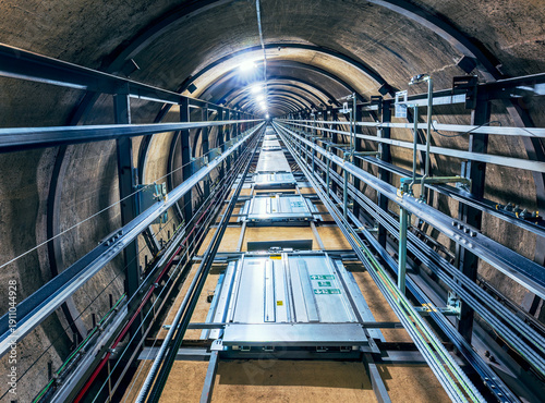 View looking upward from inside a circular elevator shaft, revealing repeating floors with elevator doors on each level.