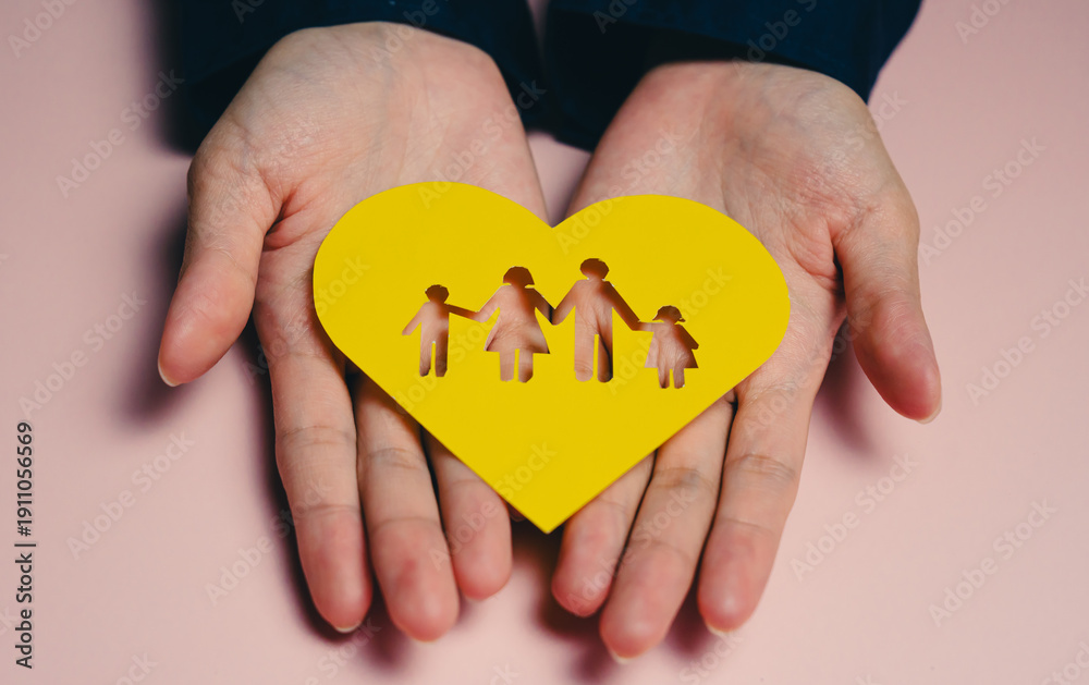 Obraz premium family concept. Hands hold yellow heart symbolizing family love and unity, featuring cut out figures of family. This conveys warmth and connection