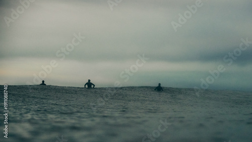 surfers sat on their boards in dark stormy seas