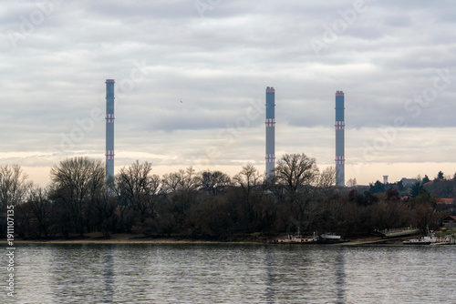 Power plant seen across the water with smokestacks and trees in the foreground during cloudy weather