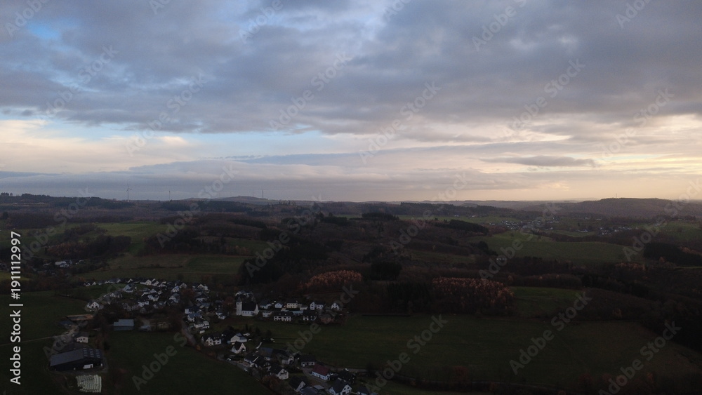 Fototapeta premium Aerial view of green rolling countryside with small village in autumn