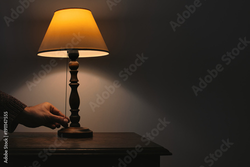 Schilderij op canvas Tactile sensory moment of a hand switching a vintage bedside lamp in the dark, creating a cozy atmosphere and warm ambient glow