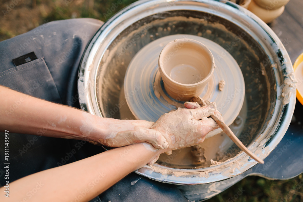 Fototapeta premium Clay pot forming on pottery wheel. Pottery shaping defines thickness, height, and symmetry before trimming and firing. Clay pot is shaped on the wheel to create stable ceramic form.