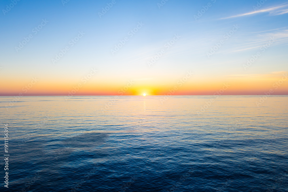 Obraz premium Tranquil fiery orange Sunrise Over ocean horizon on the Crystal Clear Caribbean Sea. Beautiful wide angle background with copy space.
