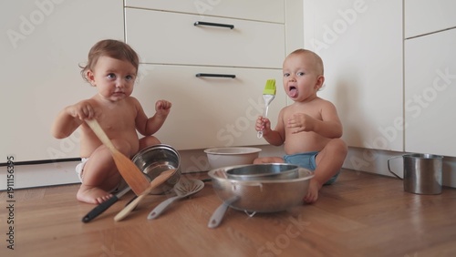 baby group playing pots in the kitchen on the floor. happy family kid dream concept. two baby twins scattered pots play dabble sitting on the floor. lifestyle baby scattered dishes pots mess
