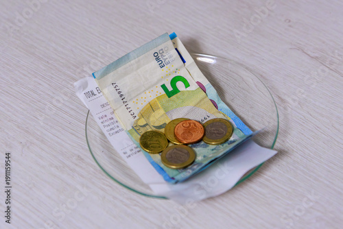 The image shows a clear glass plate placed on the table. On top of the plate are several metal coins and some carefully folded banknotes, representing the change or money given back to the customer.