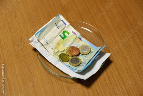 The image shows a clear glass plate placed on the table. On top of the plate are several metal coins and some carefully folded banknotes, representing the change or money given back to the customer.