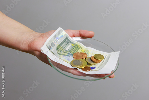 The image shows a clear glass plate in a hand; on the plate are several metal coins and some carefully folded banknotes, representing the change or money given back to the customer.
