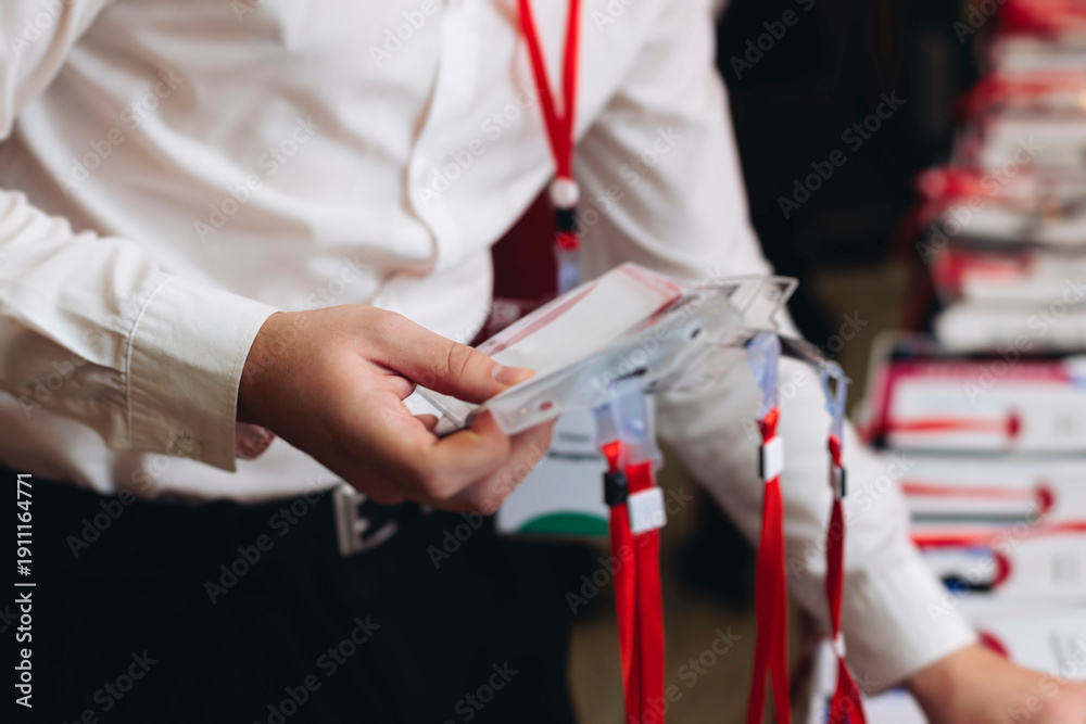 Fototapeta premium Checking in on conference congress forum event, registration desk table, visitors and attendees register electronic ticket and receiving red lanyard with name badge and entry wristband bracelet