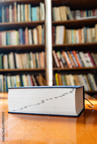Thick reference book on a wooden desk in a library with blurred bookshelves background