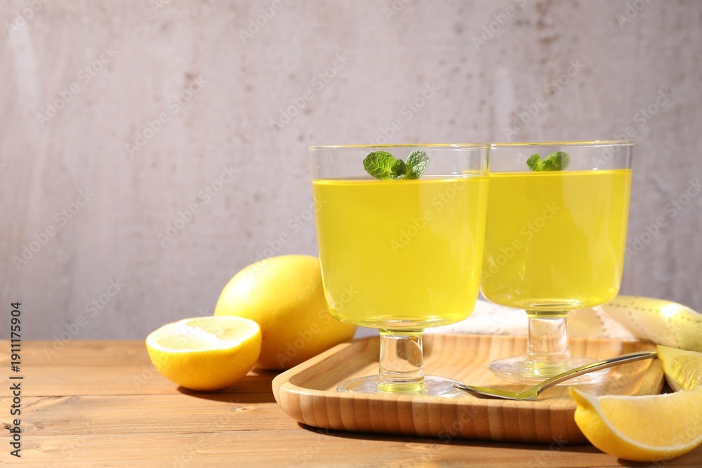 Fototapeta premium Yummy yellow jelly in dessert bowls, mint and fresh lemons on wooden table, closeup. Space for text