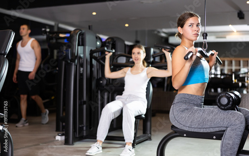 Bilde på lerret Sportive young woman doing exercises on lat pulldown training device in well-equ