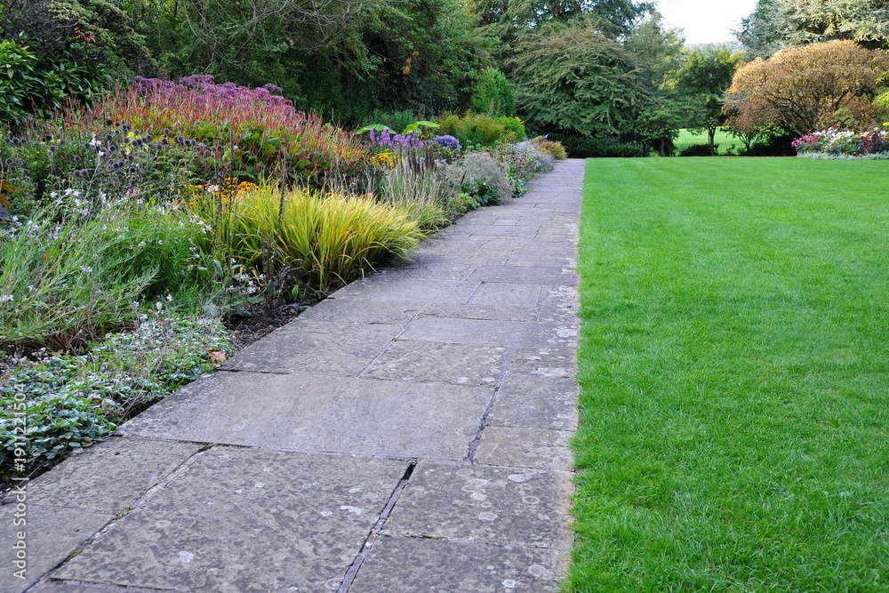 Obraz premium Stone paved path in a beautiful garden with a grass lawn and colourful flowers