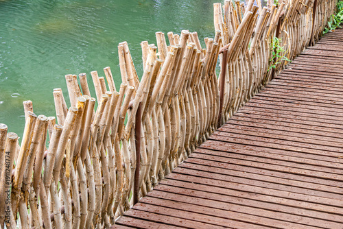 Принти на полотні Woven willow railing beside artificial pond on wooden deck in Tomsk City Garden,
