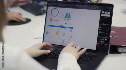 A close-up of a desk, showing the hands of an employee taking notes on a document containing graphs and data. A computer keyboard and monitor are visible. 4K.