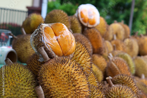 Φωτογραφία Close-up of a cut durian fruit revealing rich orange flesh wrapped in plastic, displayed on a pile of whole thorny durians at a street market