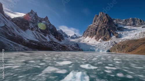 Snow covered mountains reflect in icy lake under a bright blue sky