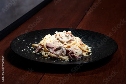 Spagetti carbonara z pieczarkami na czarnym talerzu na drewnianym stole
