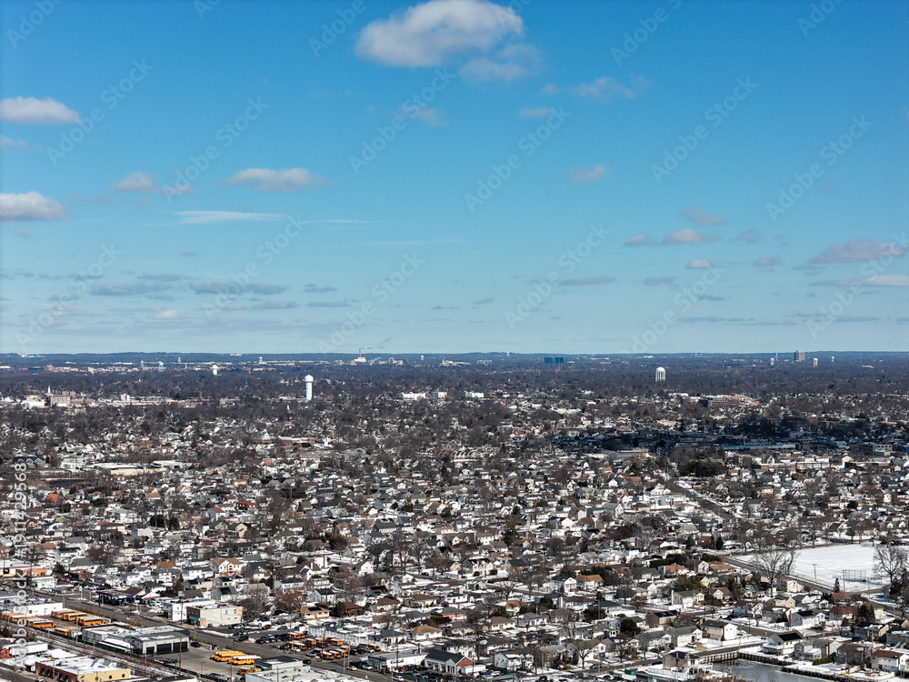 Obraz premium Aerial view of oceanside, new york suburban neighborhood blanketed in winter snow under a bright blue sky, showing rooftops, bare trees and coastal residential sprawl
