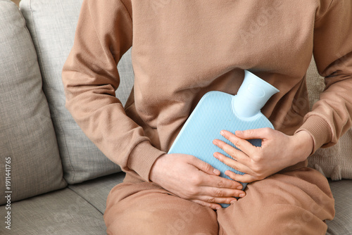 Canvas Print Woman warming her belly with hot water bottle on sofa at home