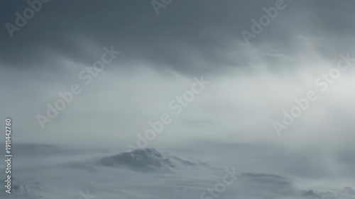 Dynamic winter landscape with winddriven snow over rolling hills and mountains under moody sky