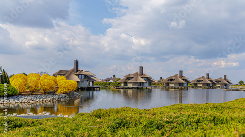 Fotografie Lakeside cottages with thatched roofs under blue cloudy sky