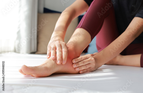 Woman massaging her painful foot with red highlight on sole and ankle. Foot pain, plantar fasciitis, muscle strain, gout and peripheral neuropathy concept for health care and physical therapy.