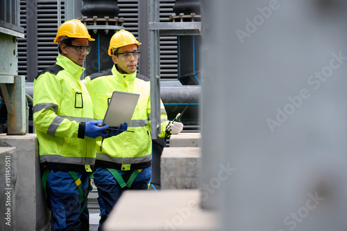 Engineers collaborate while examining a laptop, set against an industrial setting in the factory
